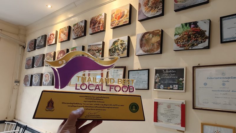 โล่ Thailand Best Local Food จากกระทรวงวัฒนธรรม ด้านหลังเป็นผนังรูปเมนูพื้นเมืองของร้าน