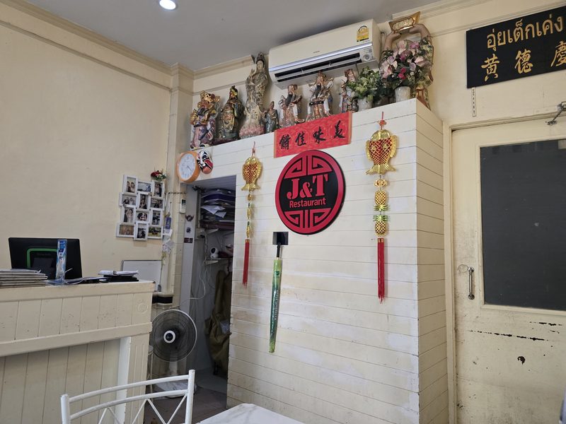 มุมในร้านเจแอนด์ที โต๊ะหินอ่อน ป้ายวงกลมสีแดง J&T และพู่มงคลแบบจีนบนผนังขาว